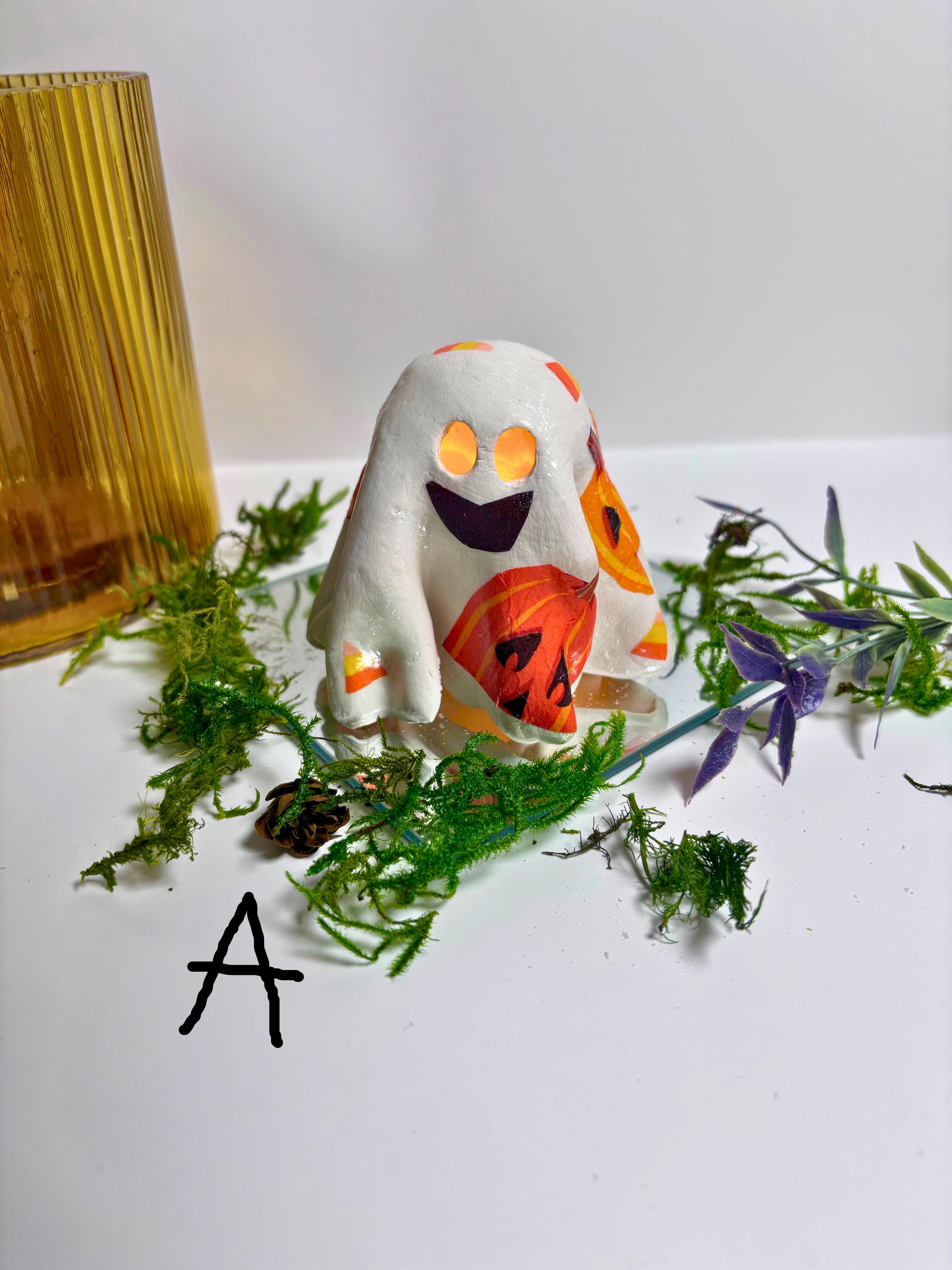 Halloween-themed ghost figurine with pumpkin face on a white surface with greenery